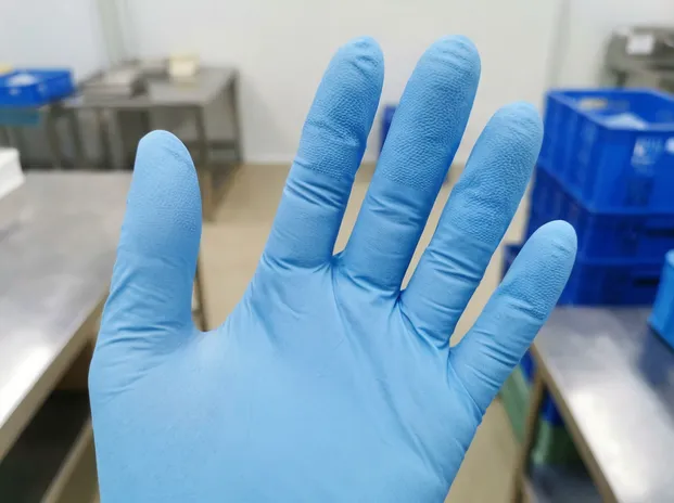 Close-up of blue nitrile exam glove showing 0.10mm palm thickness and textured fingertip detail