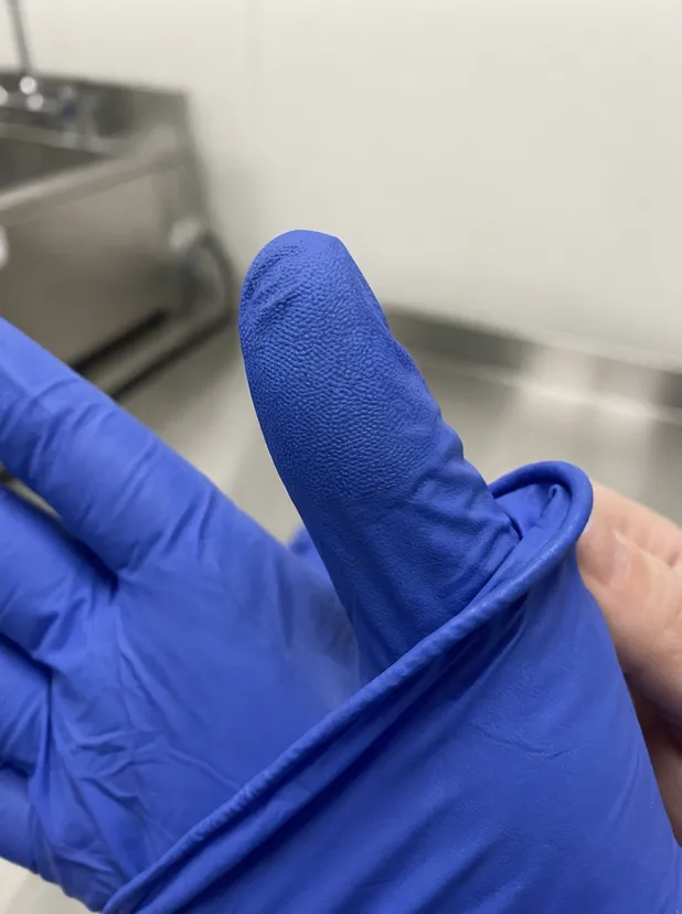 Close-up detail of cobalt blue nitrile glove showing fingertip texture and beaded cuff