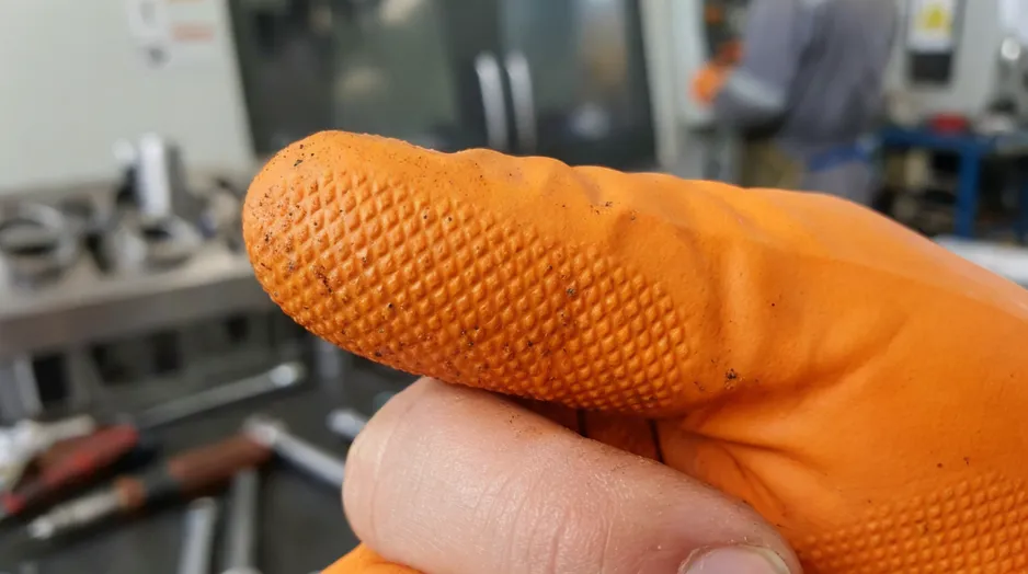 Close-up of orange nitrile glove fingertip texture — micro-pattern for grip in oily and wet environments